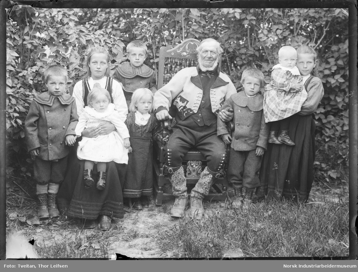 Gruppefoto. Eldre mann sittende på stol i bunad med barn rundt seg ...